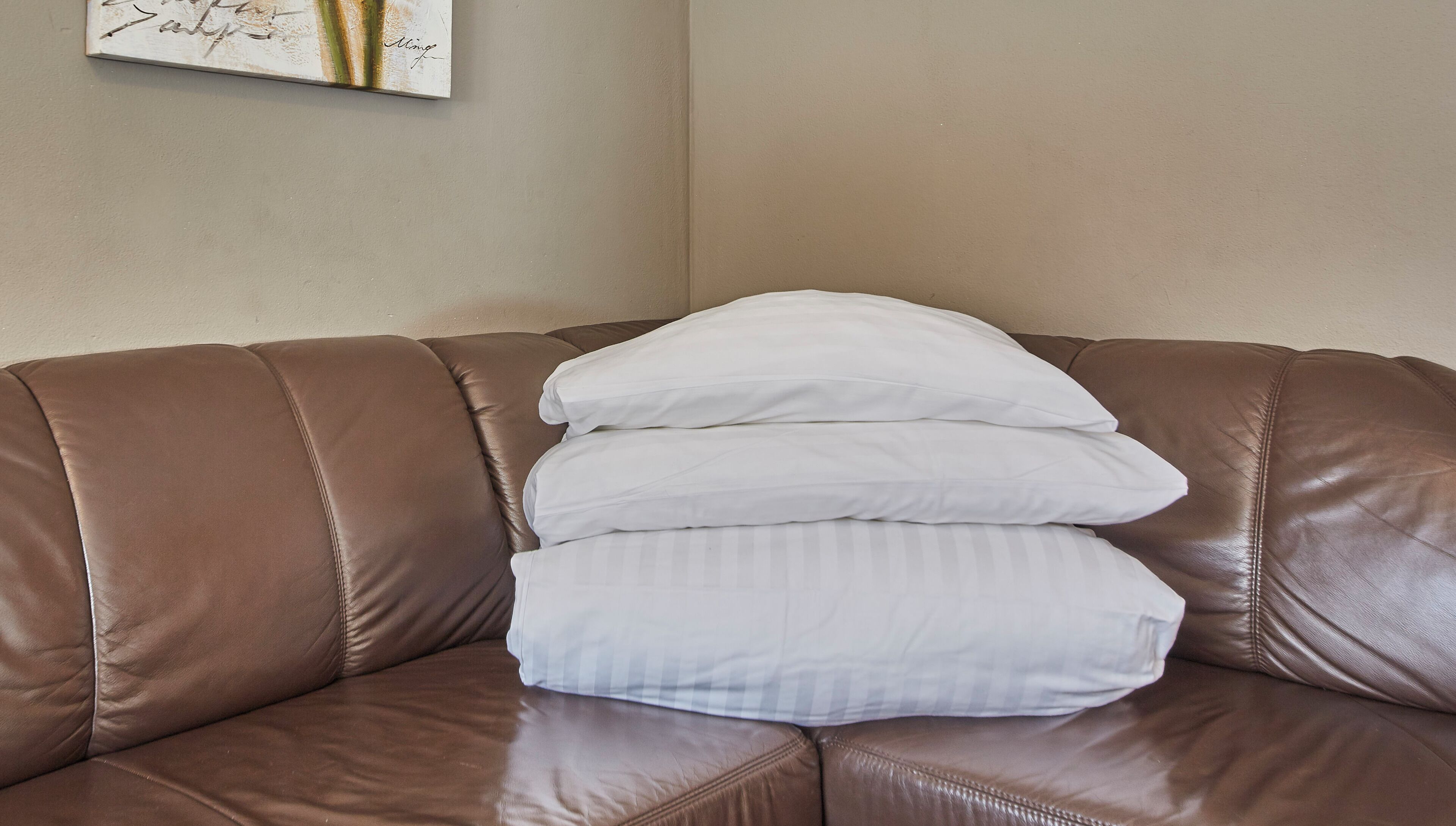 A brown leather sofa with three white pillows.