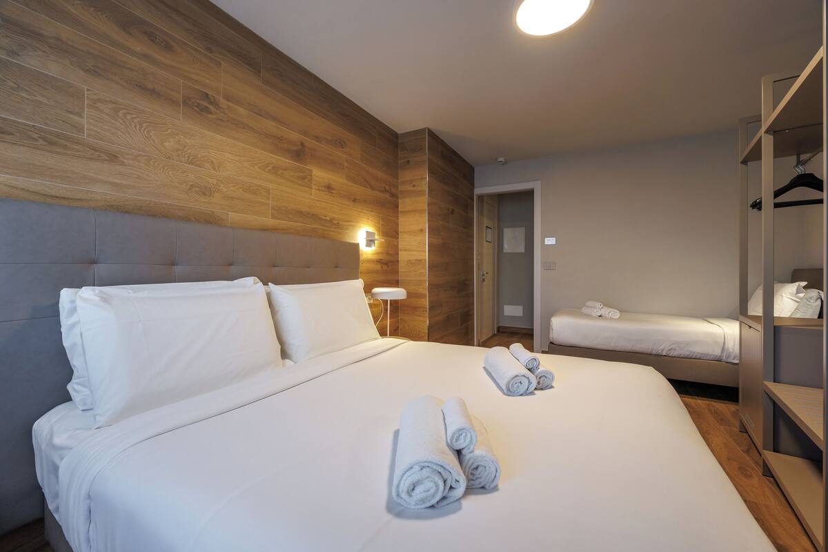 Ein Hotelzimmer mit einem großen Bett, einem kleineren Bett, einem Kleiderschrank und einer Tür zu einem anderen Raum.
