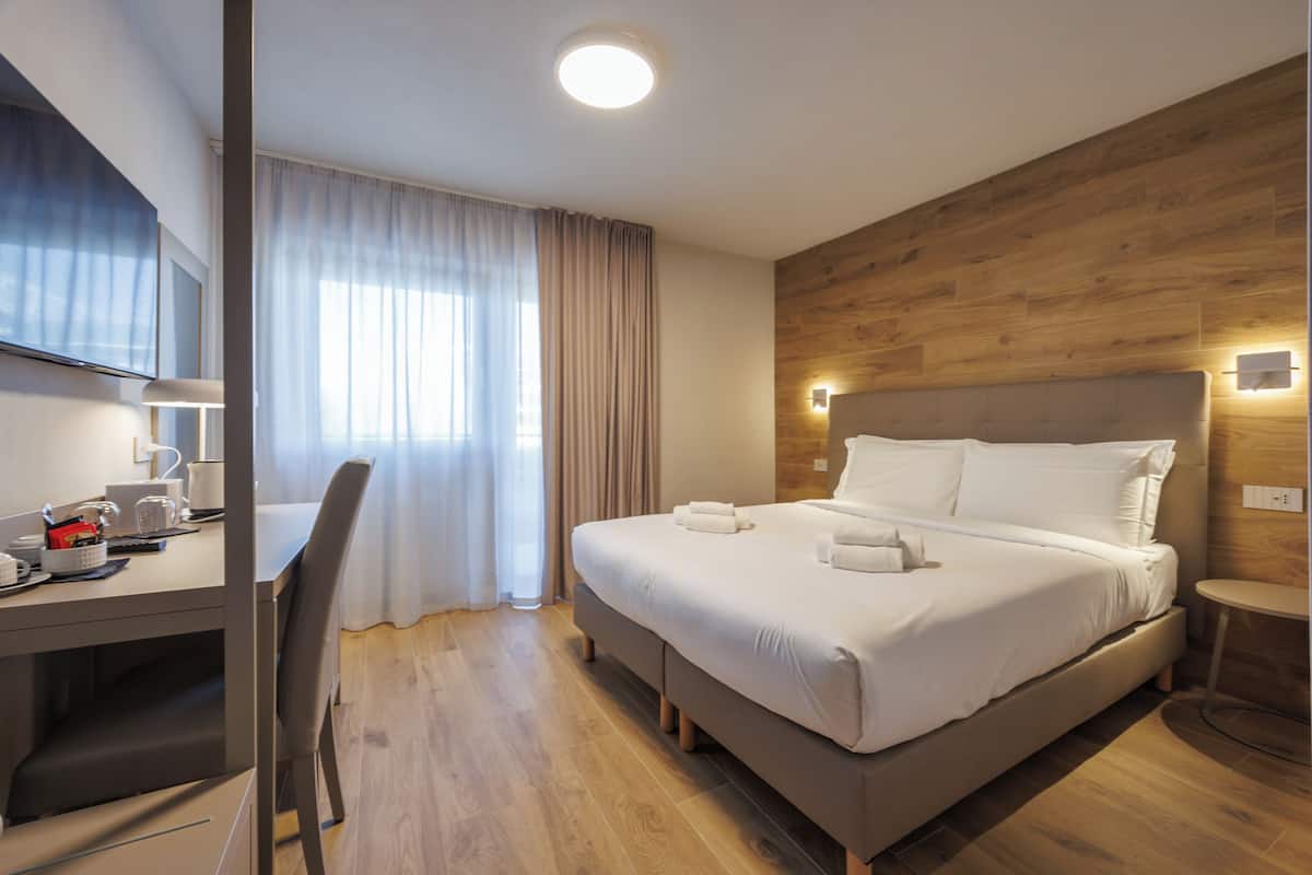 Ein modernes Hotelzimmer mit einer Wandpaneele aus Holz, einem großen Bett mit weißen Leinen, einem Schreibtisch mit Stuhl und einem Fernseher.