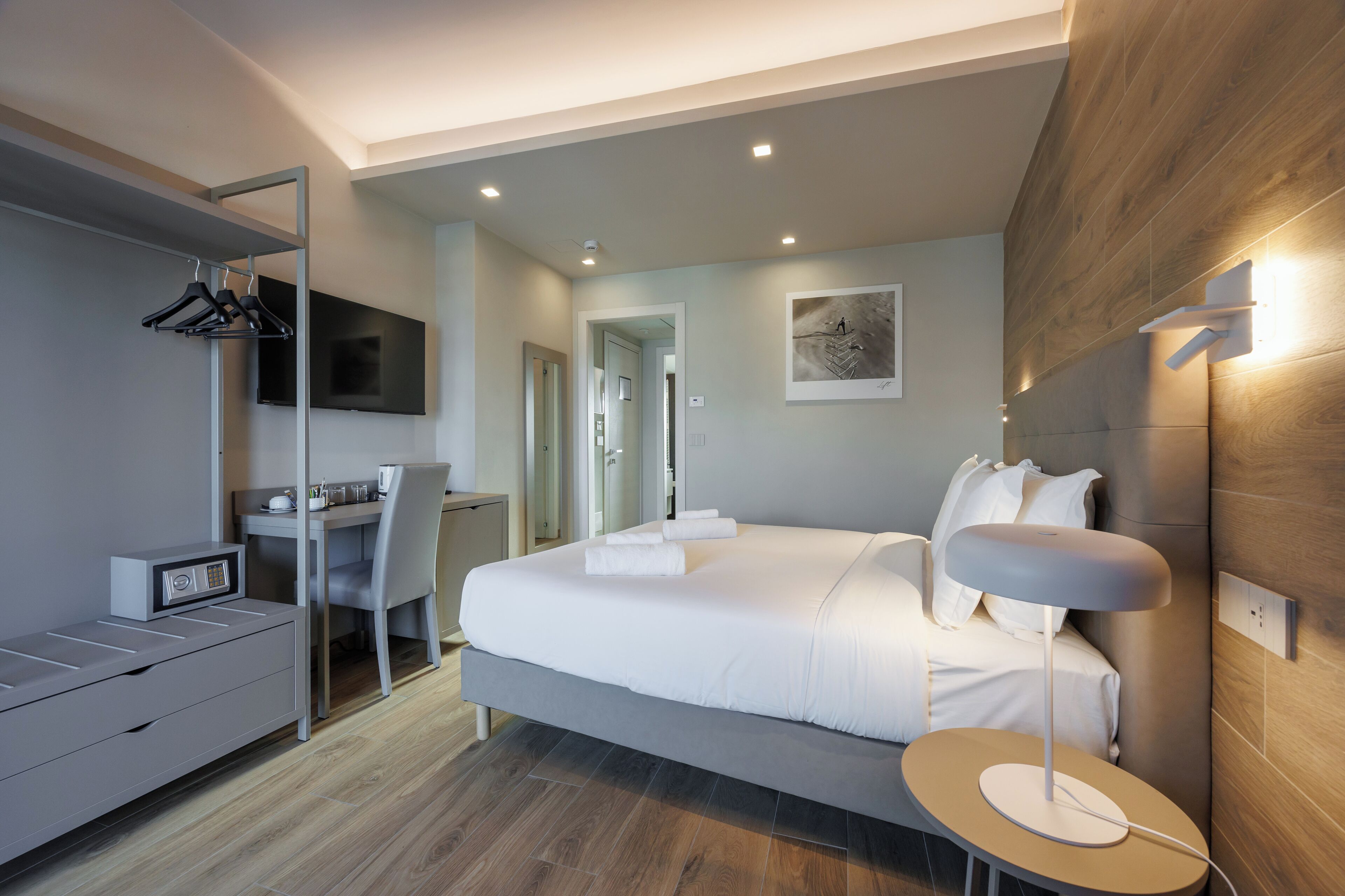 Un dormitorio moderno con cama, mesita de noche, escritorio, silla y televisor montado en la pared.