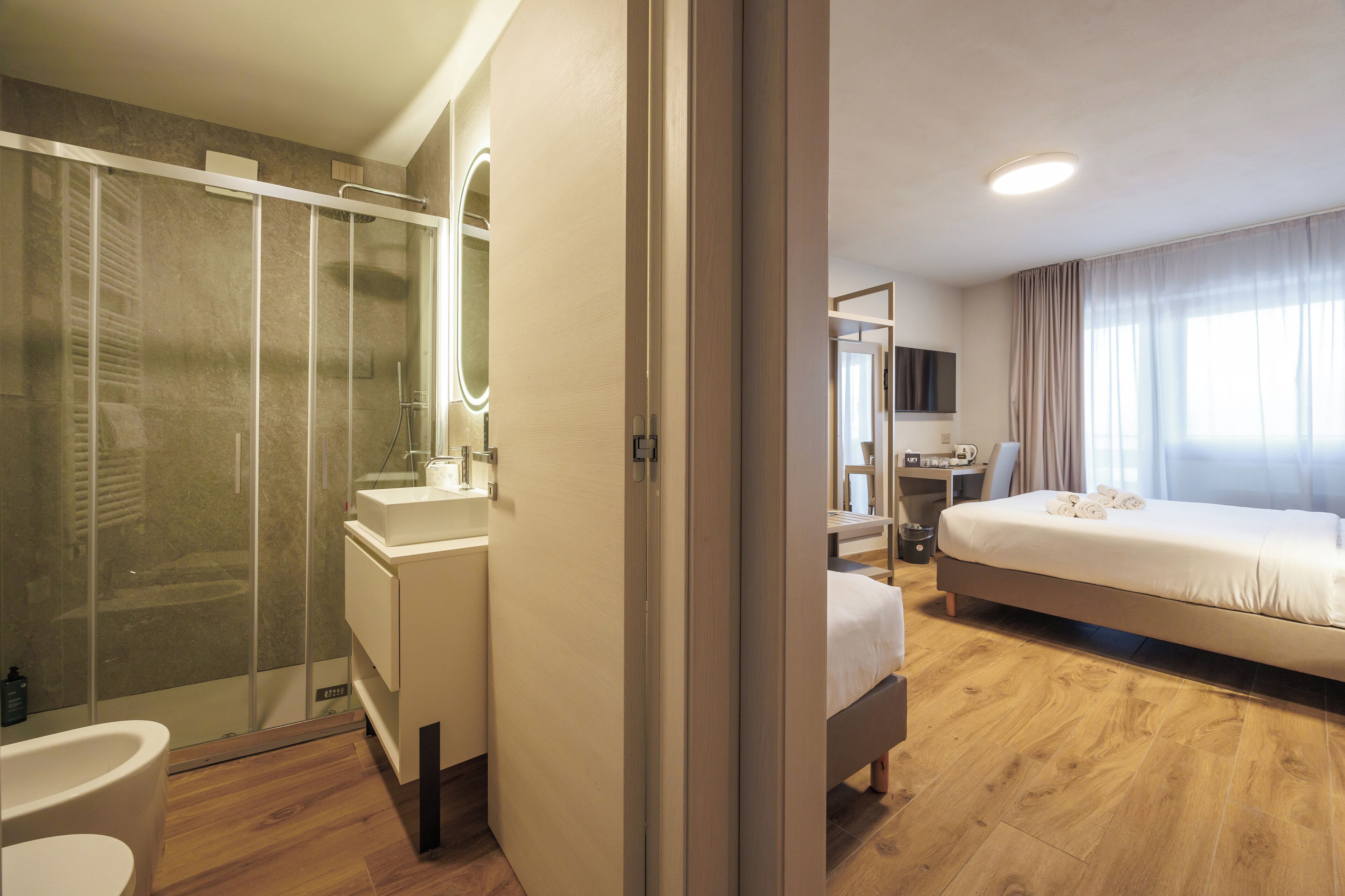 A modern hotel room with a shower, sink, and a bed with towels.