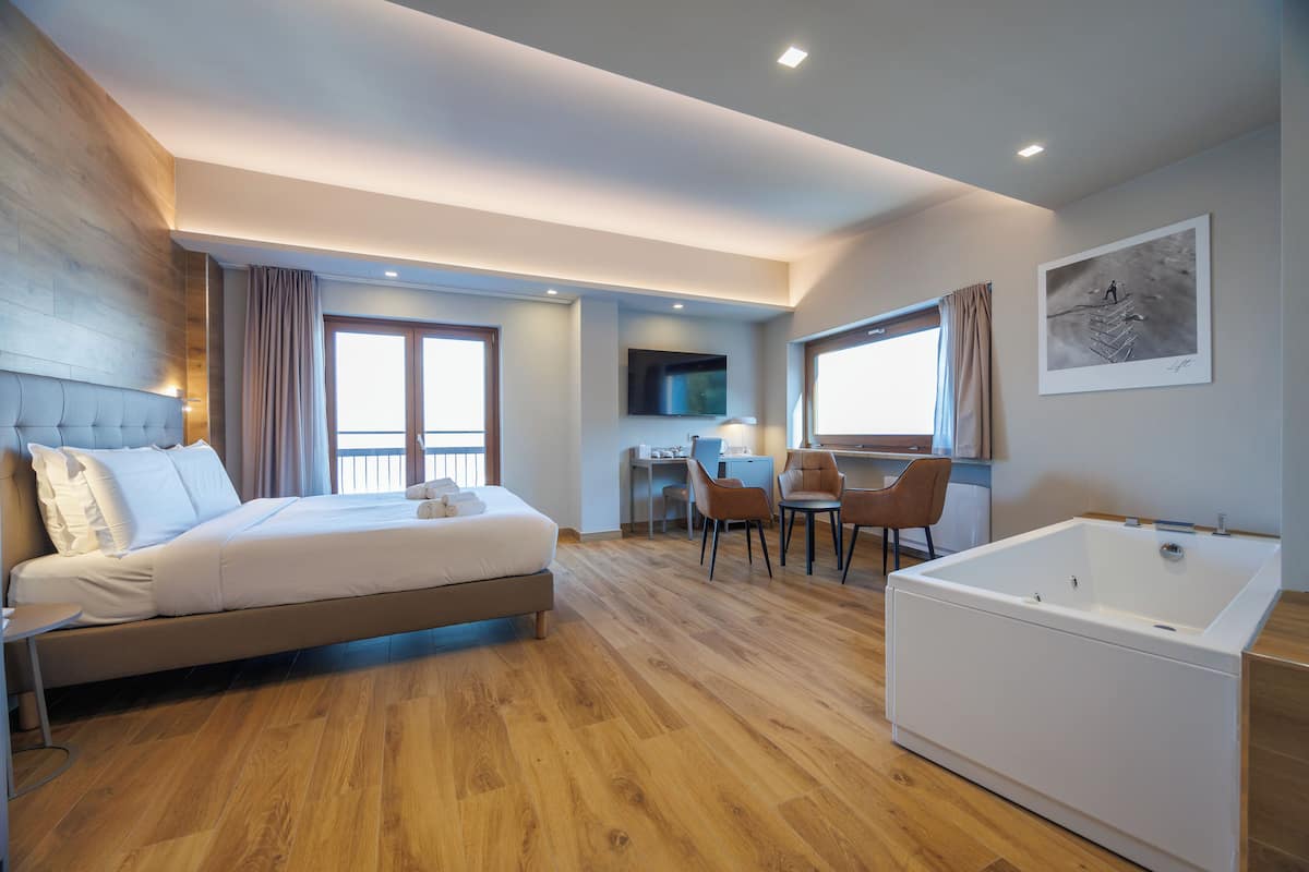 Ein modernes Hotelzimmer mit einem großen Bett, einer Sitzecke mit Schreibtisch und Stühlen, einer Badewanne und einem Fernseher an der Wand.