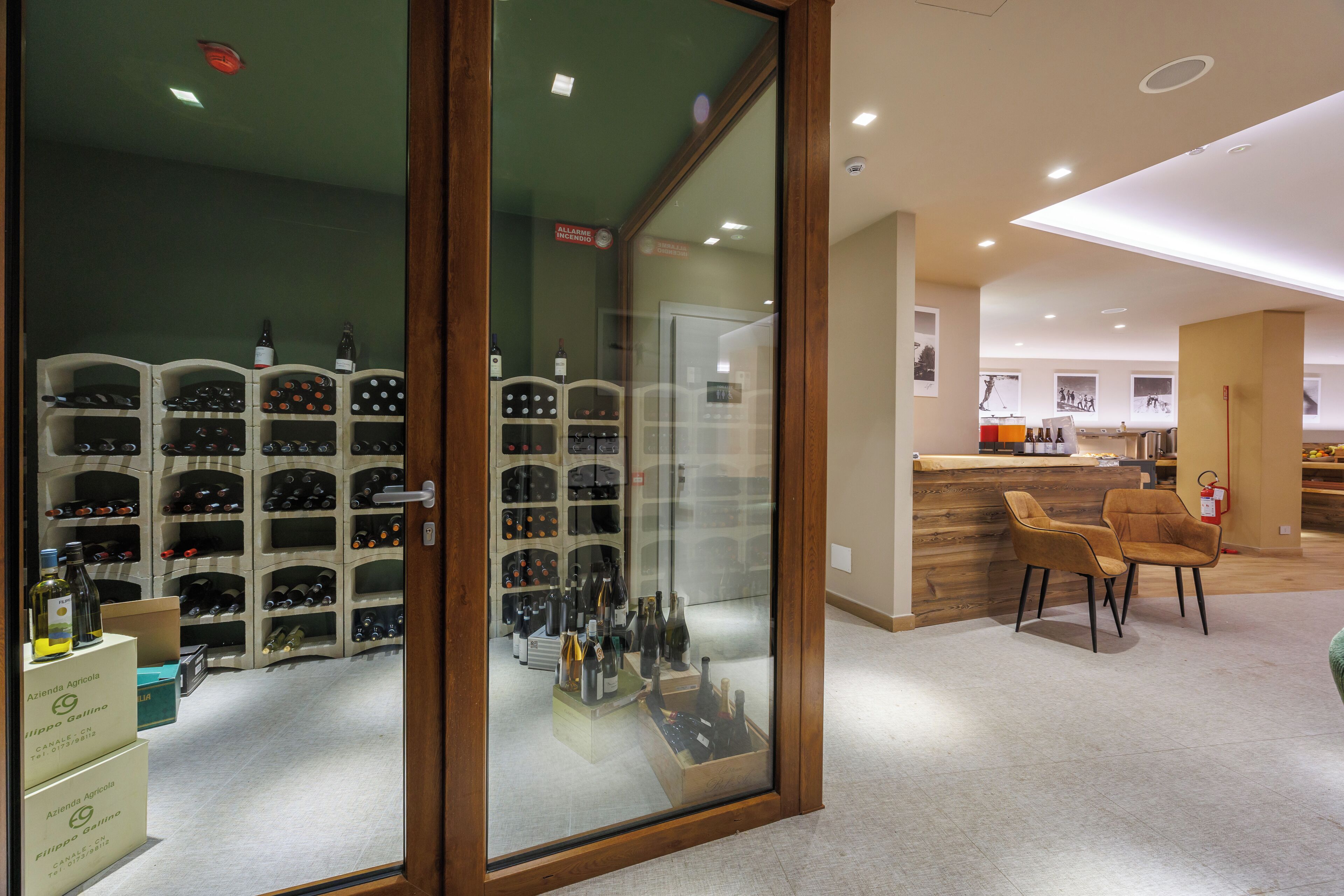 A wine cellar with multiple racks of wine bottles, a reception area with a wooden counter, and a seating area with chairs.