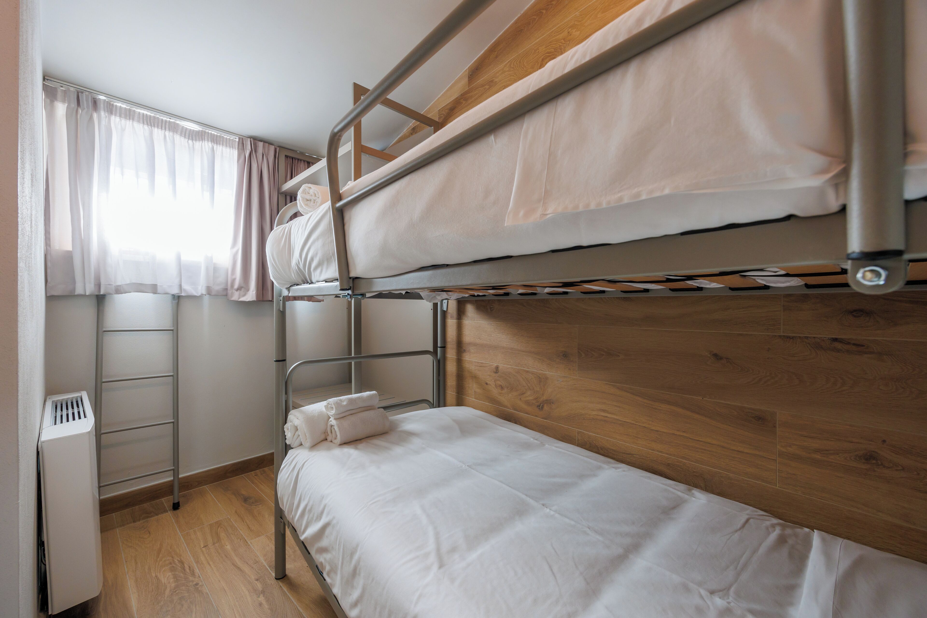 A bunk bed room with a wooden headboard, a window with curtains, and a radiator.