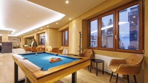 A pool table with a blue felt surface, surrounded by modern chairs and a view of a snowy landscape through large windows. - Lift Hotel  (Sauze d'Oulx)
