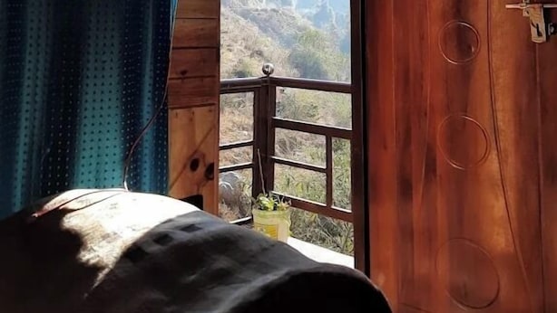 A bedroom with a wooden door, a bed, and a window with a view of mountains. - SANDEEP HOME STAY (Chakrata)