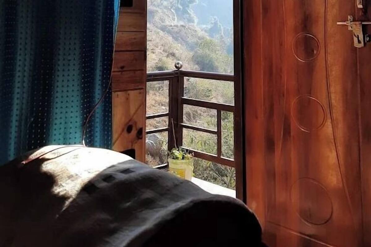 A bedroom with a wooden door, a bed, and a window with a view of mountains.