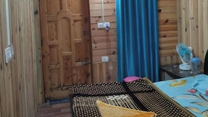A small, wooden room with a bed, a desk, and a window with curtains. - SANDEEP HOME STAY (Chakrata)
