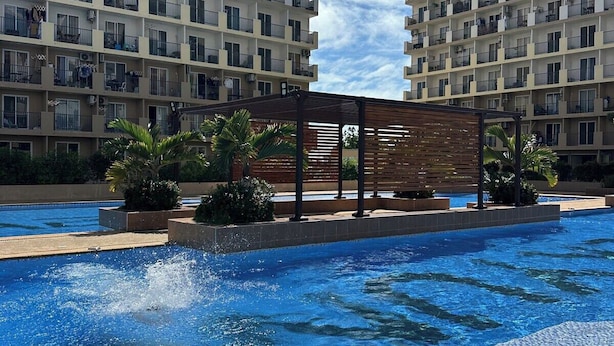 A swimming pool with a wooden deck and palm trees, surrounded by high-rise residential buildings. - Nicosia's Place (Lapu-Lapu)