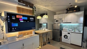 A modern kitchen with a built-in TV displaying a streaming service interface, a washing machine, and a compact dining area. - Nicosia's Place (Lapu-Lapu)