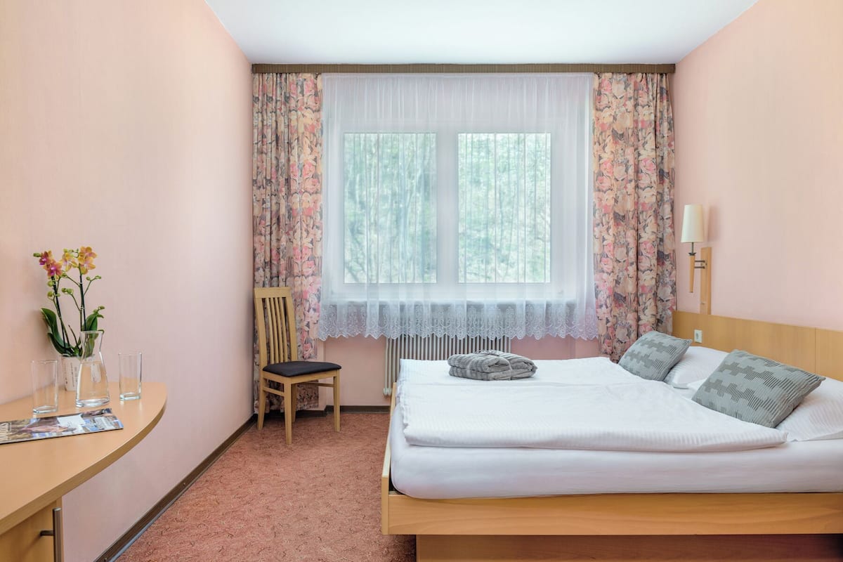 A hotel room with a bed, a chair, a table, and a window with curtains.