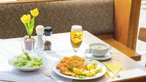 A dining table with a plate of schnitzel, salad, lemon wedges, and a cup of soup. There are also condiments, a salt and pepper shaker, and a glass of beer.