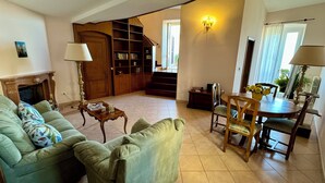 Un salon comprenant un canapé, une table, une lampe, une cheminée, une bibliothèque et un escalier menant à une autre pièce.