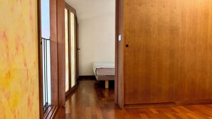 Un couloir étroit avec un plancher en bois, une porte coulissante en verre et un lit recouvert d’une courtepointe à rayures.