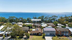 A residential area with houses, a sign reading 'Solace Jervis Bay,' and a view of the ocean. - Solace Jervis Bay - 3BR relaxed beach side living (Vincentia)