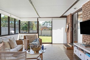 A spacious patio with a sofa, a table, and a TV. - Solace Jervis Bay - 3BR relaxed beach side living (Vincentia)