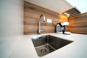 Eine moderne Küche mit Spüle aus Edelstahl, Holzrückwand und einer Kaffeemaschine.