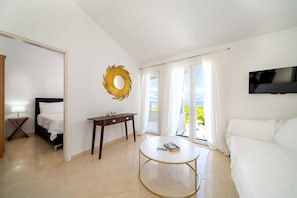 Ein modernes Hotelzimmer mit Bett, rundem Tisch, Fernseher und Blick ins Freie.