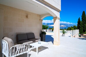 Uma área de estar externa com uma mesa branca e um sofá marrom, uma planta em vaso e vista para montanhas e uma piscina.