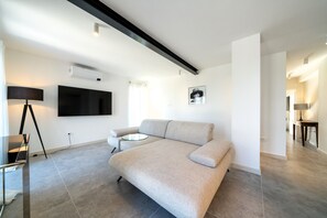 Uma sala de estar moderna com um sofá, uma mesinha redonda, um abajur e uma televisão de tela plana fixada na parede.