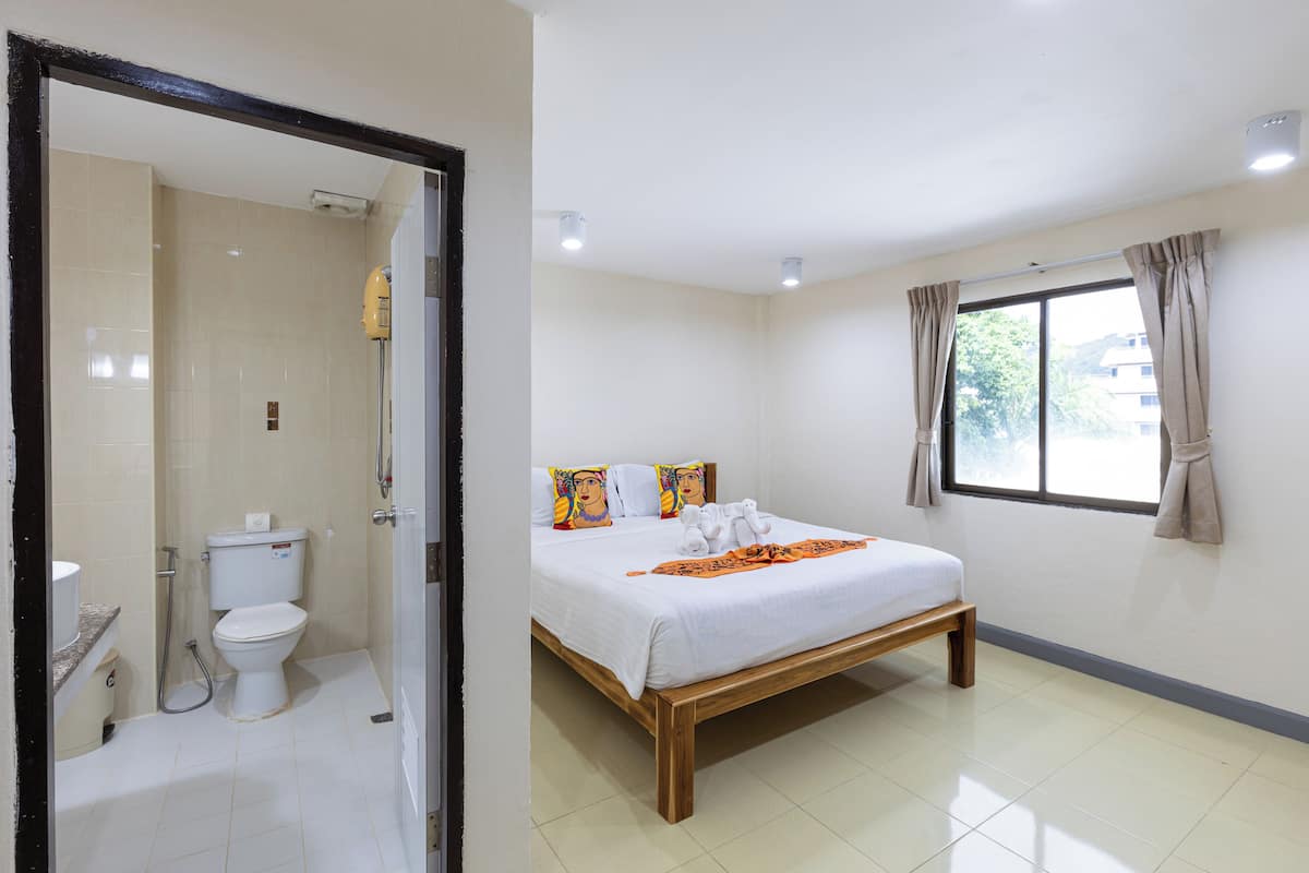 A bedroom with a bed, a window with curtains, a bathroom with a toilet, and a shower.