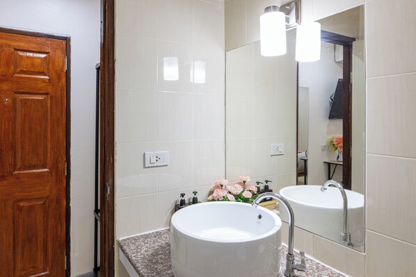 Un baño con puerta de madera, paredes de azulejos blancos, un lavamanos blanco y un espejo encima, además de una lámpara.