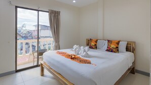 Une chambre d’hôtel avec un grand lit, un balcon donnant sur des immeubles et une tête de lit en bois.
