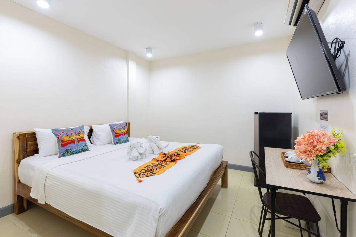 A hotel room with a bed, a desk, a chair, a TV, and a vase with flowers.