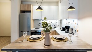 A modern kitchen with a wooden table, two pendant lights, a stainless steel refrigerator, and a coffee maker. - The Beatles 2-BR Apartment in Athens (Athens)