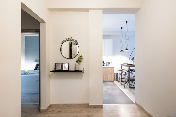 A hallway with a mirror, framed pictures, and a small plant on a shelf. There is a bed visible in the background. - The Beatles 2-BR Apartment in Athens (Athens)