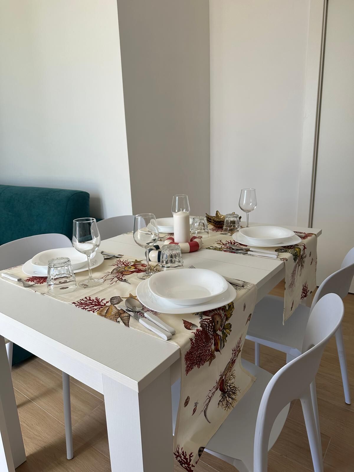 A dining table set with white plates, glasses, and cutlery, covered by a floral tablecloth.