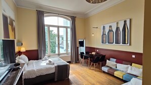 Une chambre d’hôtel comprenant un lit, un canapé, une table à manger, un coin cuisine et une grande fenêtre avec des rideaux.
