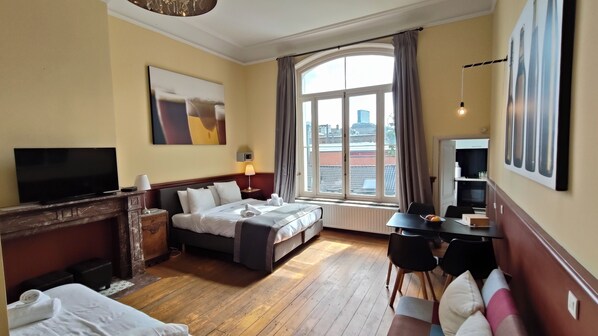 A hotel room with a bed, a TV, a desk, and a window with a city view.
