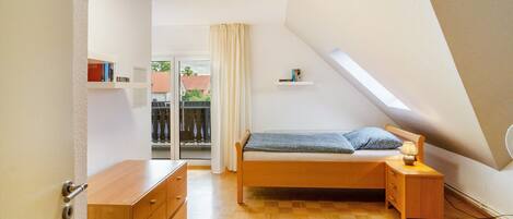 A bedroom with a bed, bedside table, dresser, and a window with a view of the outside.
