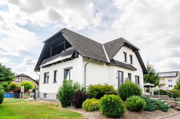 A modern two-story house with a sloped roof, a visible attic, and a well-maintained garden with various shrubs and a lawn.
