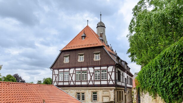 A traditional half-timbered building with a steeply pitched roof, a visible tower, and a cobblestone pathway.