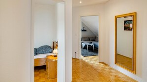 A room with a bed, bedside table, lamp, and a large mirror on the wall.