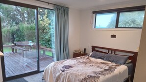 Ein Schlafzimmer mit einem großen Bett, einem Nachttisch, einem Fenster und einer Glastür, die auf eine Terrass geht.
