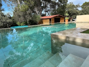 A clear swimming pool with a wooden structure in the background, surrounded by trees.