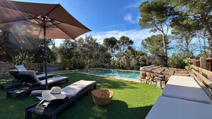 Un espace aménagé au bord de la piscine, avec des chaises longues, un parasol et un mur en pierre.