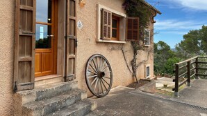 Un bâtiment rustique avec une porte en bois, deux fenêtres avec volets, une grande roue et un escalier en pierre.