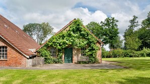A brick building with a green door, ivy-covered roof, and a grassy lawn. - Country House 'Friesenhof' with Shared Terrace, Private Garden, and Wi-Fi (Wangerland)