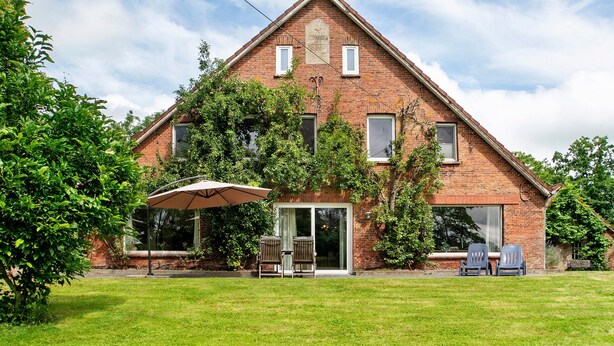 A brick house with a triangular roof, a front door, and a patio with two chairs and an umbrella. - Country House 'Friesenhof' with Shared Terrace, Private Garden, and Wi-Fi (Wangerland)