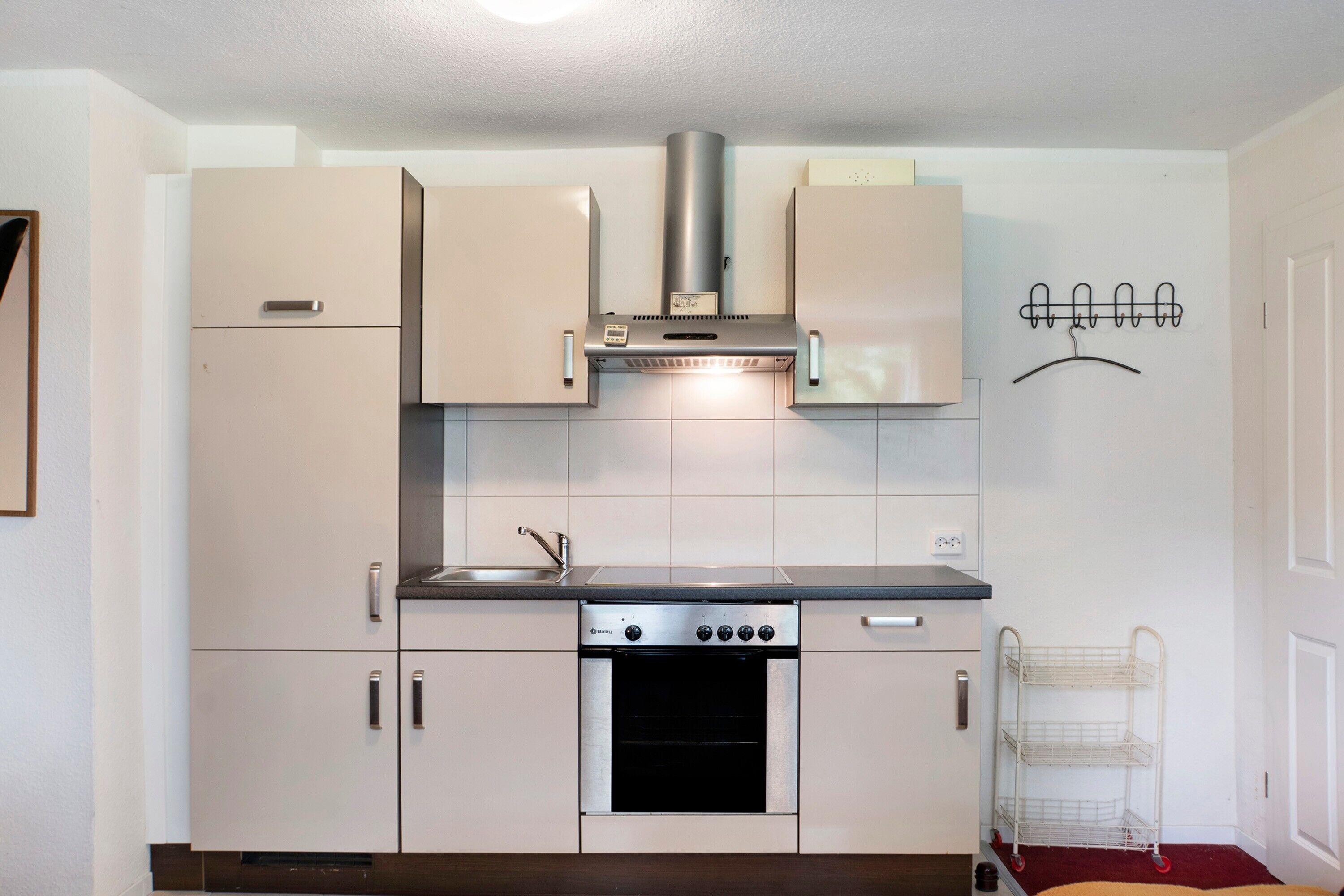 Eine kompakte Küche mit Backofen, Edelstahl-Dunstabzugshaube und einer Kleiderstange.
