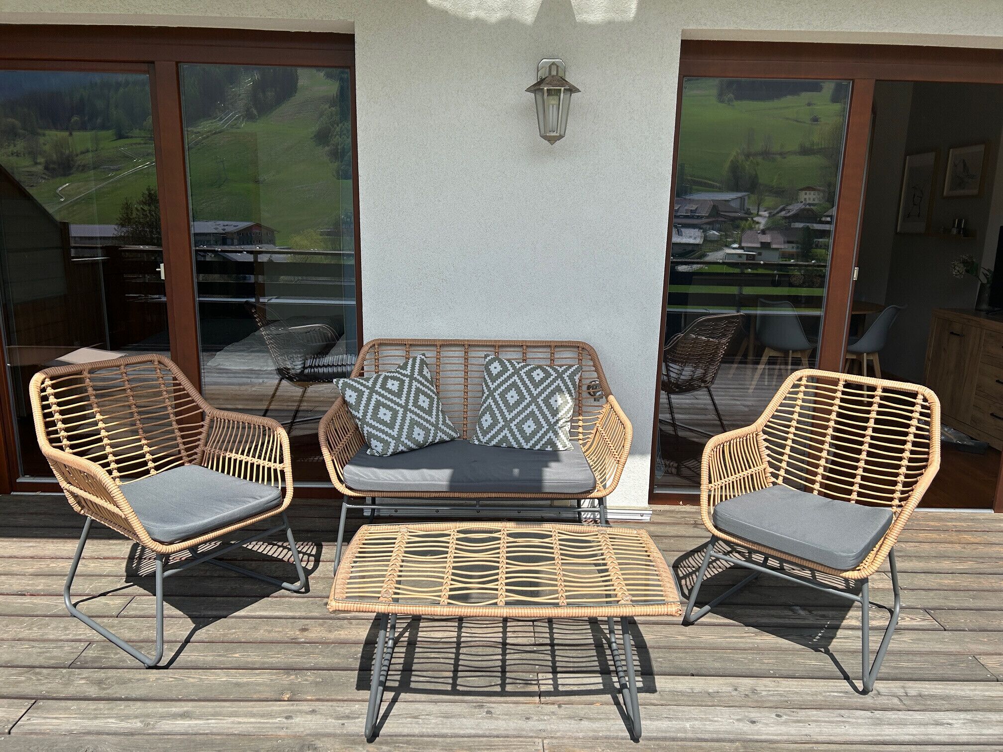 Una terraza con mobiliario de mimbre, incluyendo dos sillones y un sofá con cojines, y una mesita.