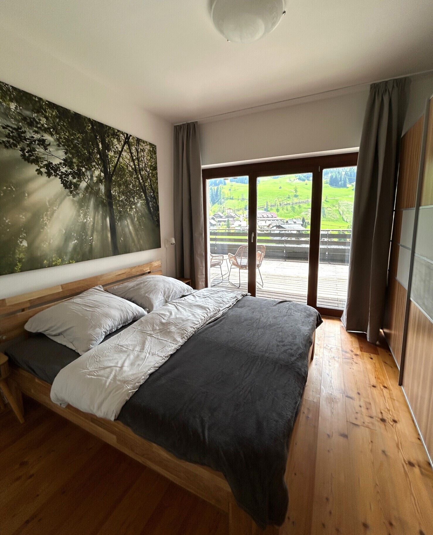 Un dormitorio con una cama grande, vista a un paisaje verde a través de una puerta corredera y un cuadro de árboles en la pared.