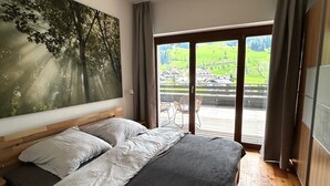 Un dormitorio con una cama grande, vista a un paisaje verde a través de una puerta corredera y un cuadro de árboles en la pared.