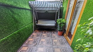 Egy kis, zárt, szabadtéri ülősarok, mintás padlóval, csíkos napellenzővel és virágtartóban elhelyezett növényekkel.