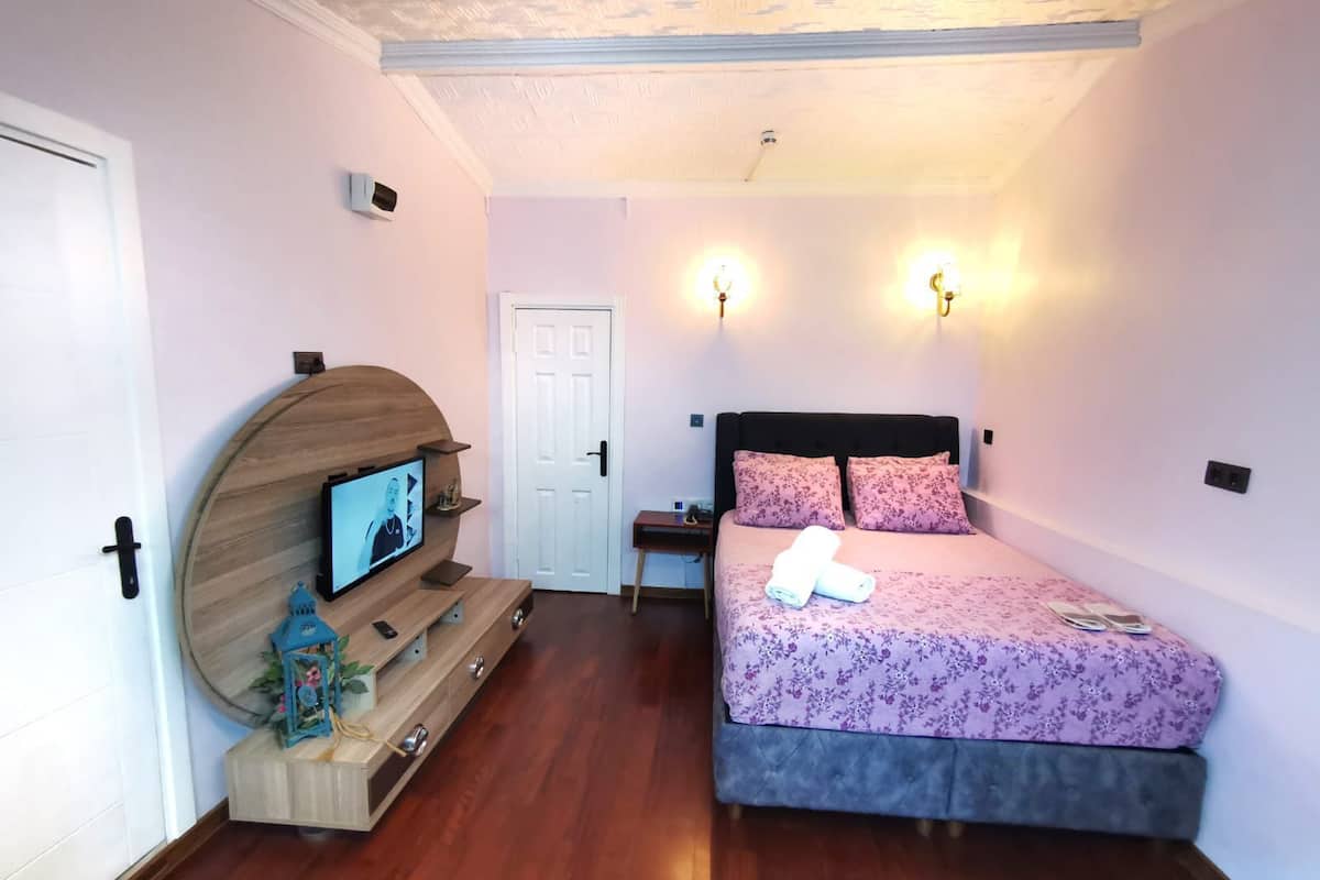 Ein Schlafzimmer mit einem Bett, einem Fernseher auf einem Holzboden, einer Tür und zwei Wandleuchten.