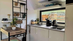 Una cocina compacta con ventana, armarios blancos, una mesa de madera y diversos utensilios de cocina.